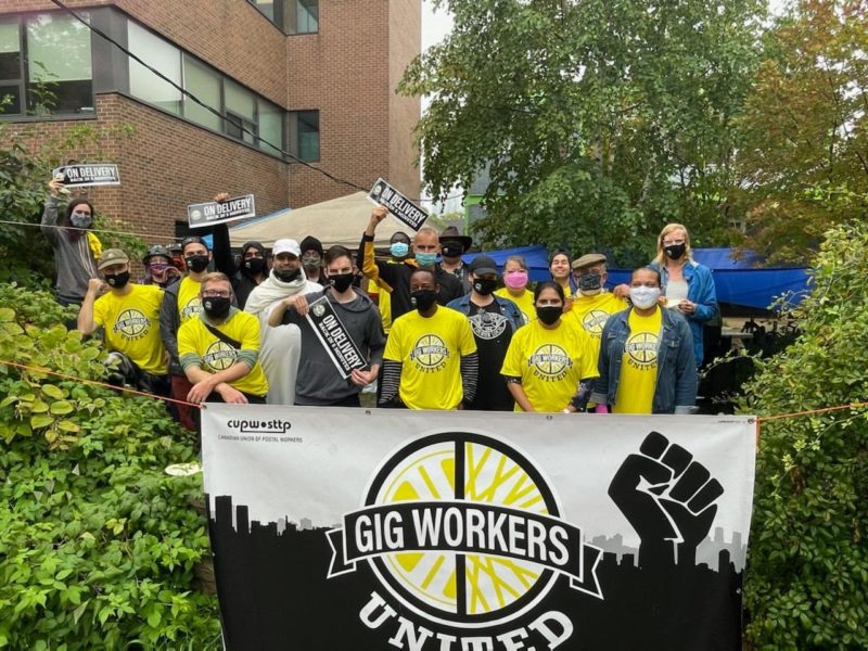 Photo of a group of people wearing yellow gig workers united shirts standing behind a gig workers united banner