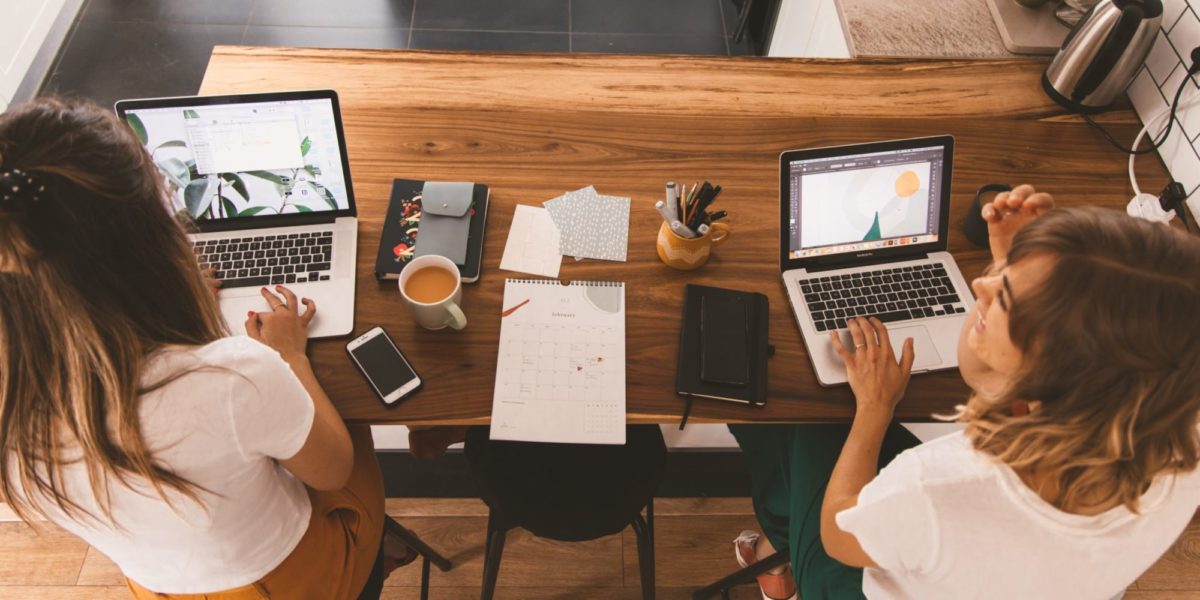 A stock photo of two women working on their computers and talking to each other.