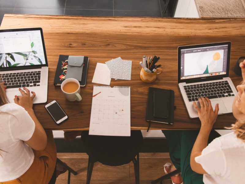 A stock photo of two women working on their computers and talking to each other.