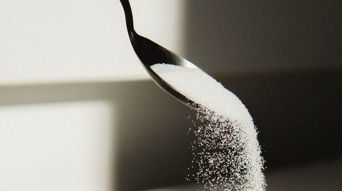 Photo of white sugar being poured from a spoon into a bowl