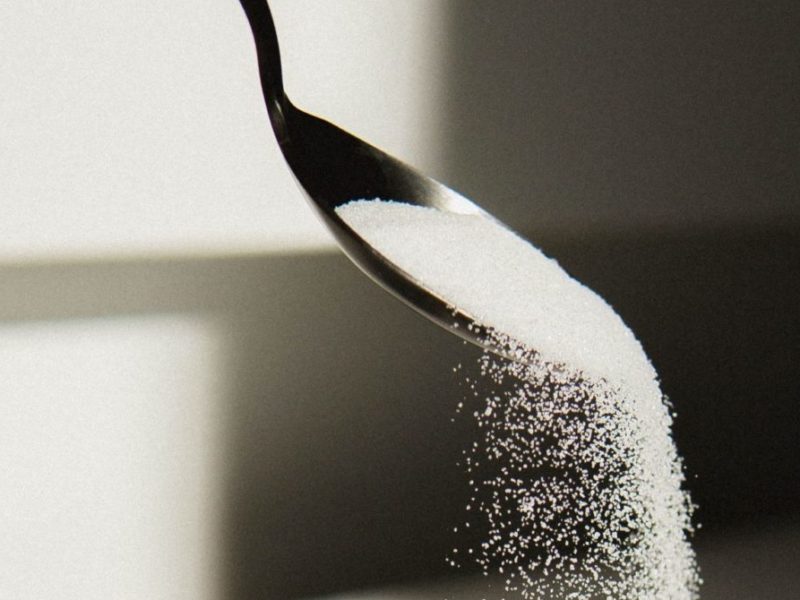 Photo of white sugar being poured from a spoon into a bowl