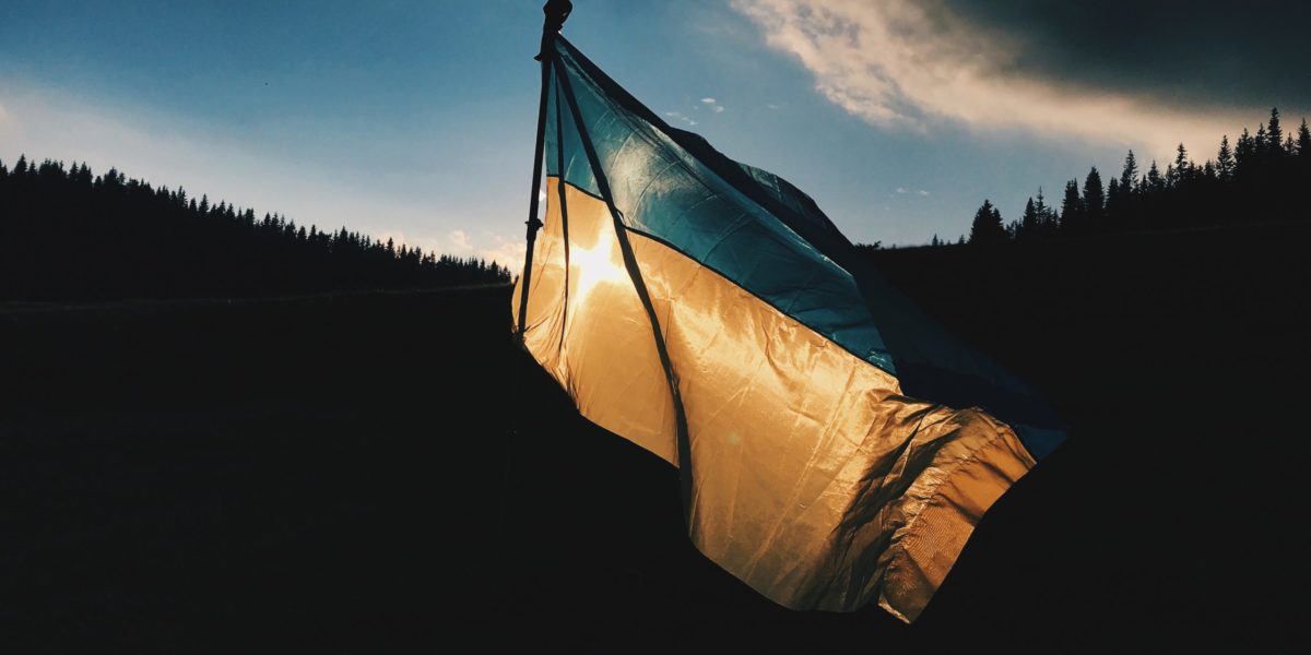 Photo of the Ukrainian flag flying on a backdrop of forest and sunset.