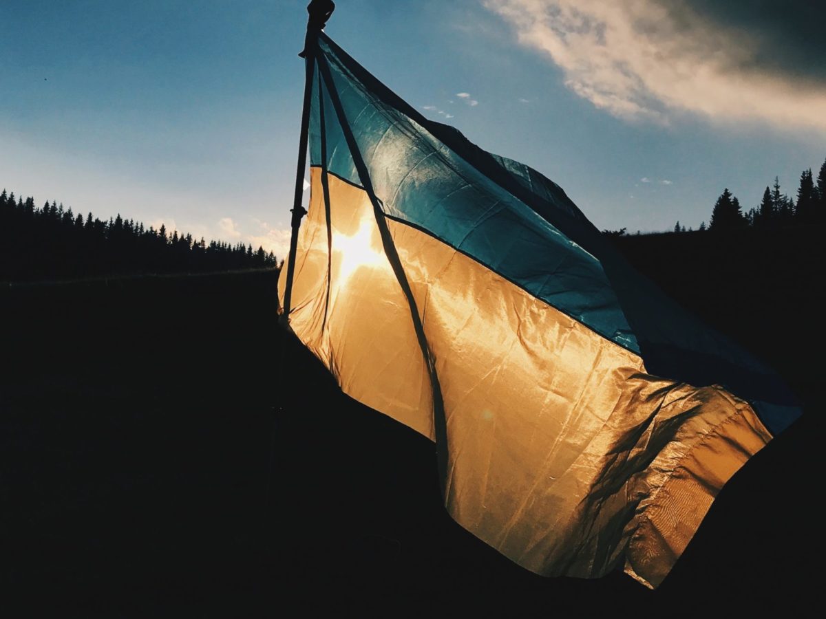 Photo of the Ukrainian flag flying on a backdrop of forest and sunset.