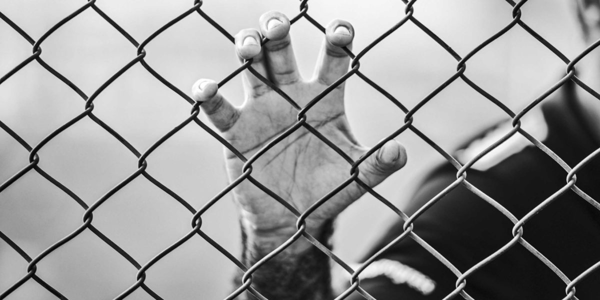 Photo of a person behind a barbed wire fence.