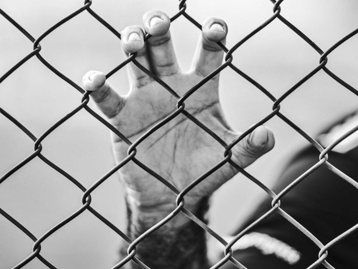 Photo of a person behind a barbed wire fence.