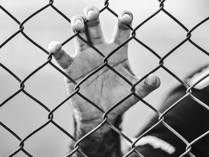 Photo of a person behind a barbed wire fence.