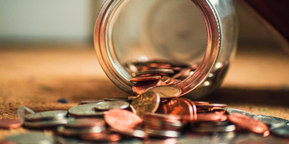 A photo of a glass jar of pennies tipped over and spilling on a table.