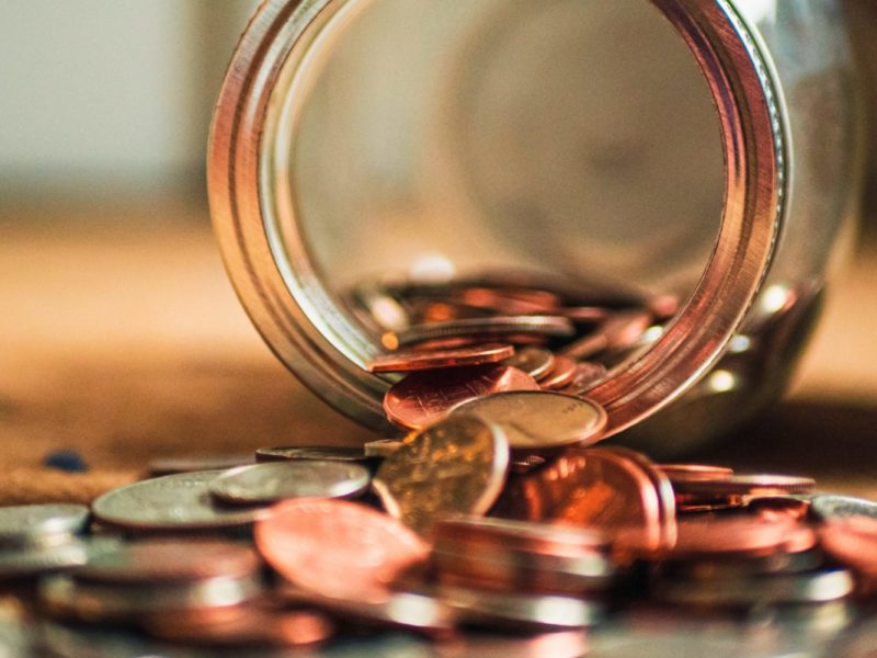 A photo of a glass jar of pennies tipped over and spilling on a table.