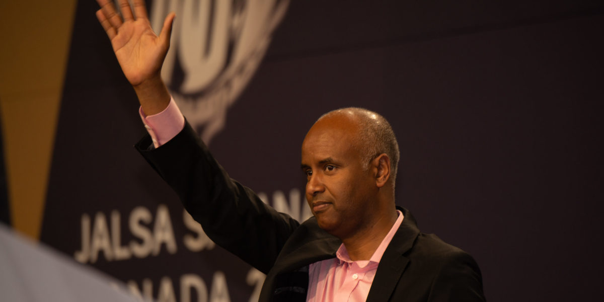 A photo of Ahmed Hussen standing at a podium waves hand.