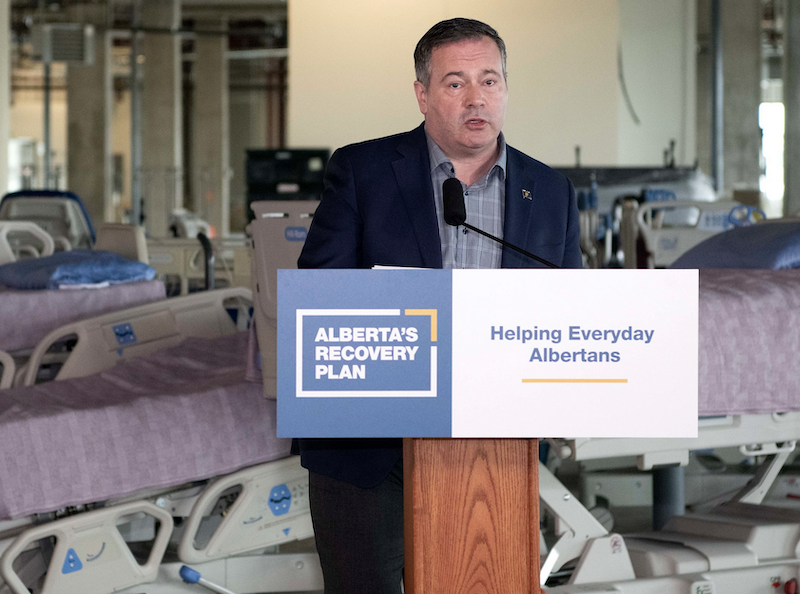 A photo of A tired-looking Jason Kenney at yesterday’s news conference on what looks like the set of a minimalist post-modern theatre production.