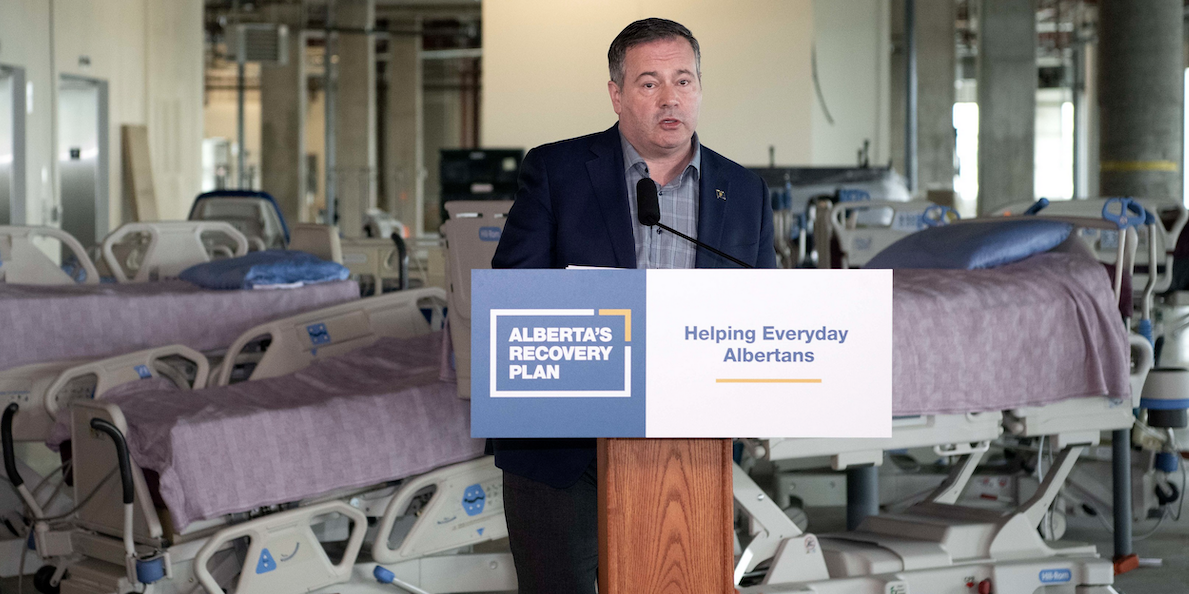 A photo of A tired-looking Jason Kenney at yesterday’s news conference on what looks like the set of a minimalist post-modern theatre production.