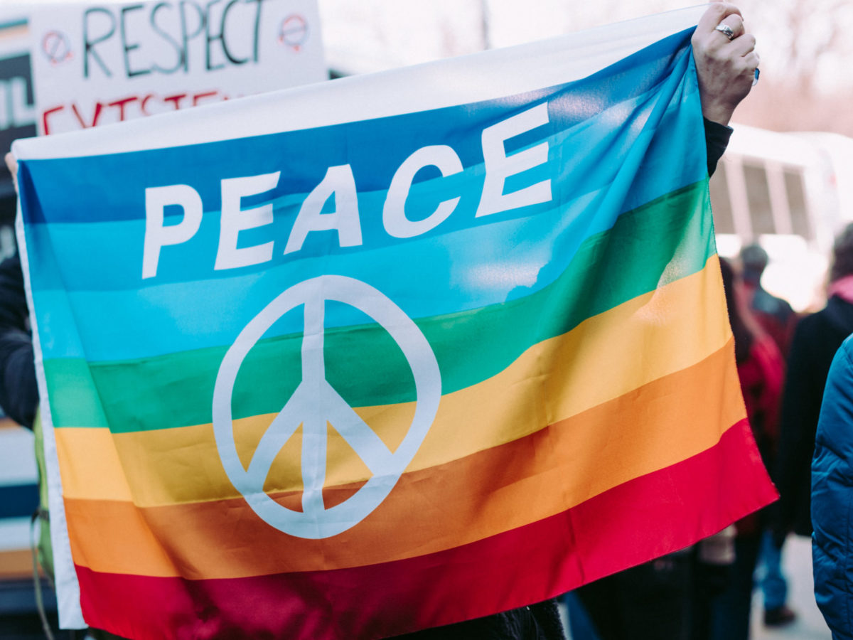 A photo of a rainbow flag with the peace sign on it.