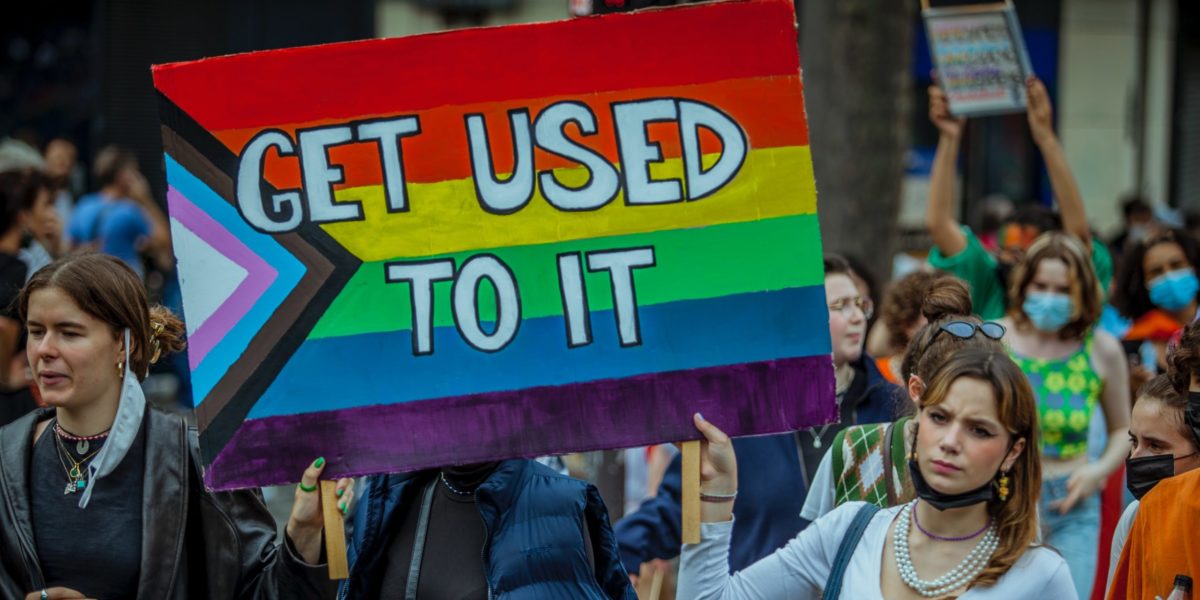 A sign with the LGBTQIA+ flag which says "Get used to it"