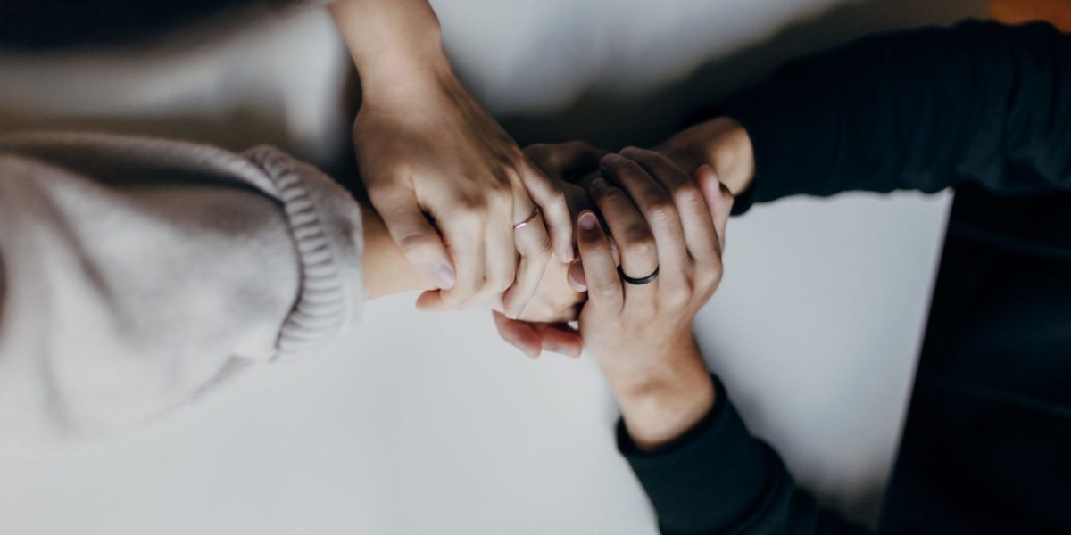 A photo of two people clasping hands over a table, offering support to one another.