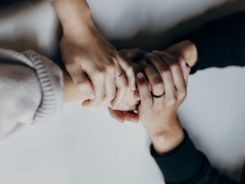 A photo of two people clasping hands over a table, offering support to one another.