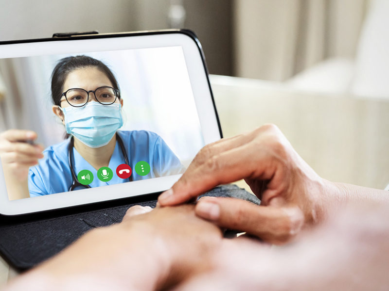 Image of a woman wearing a medical mask displayed on a phone screen with a set of hands in front of it.