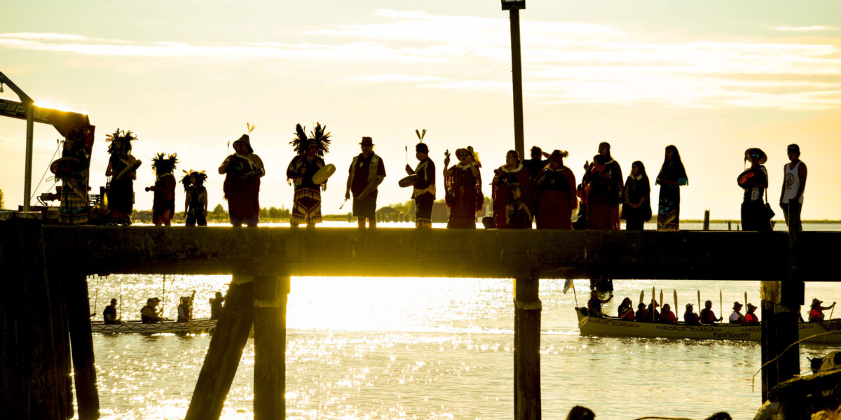 A photo of a Indigenous peoples holding a ceremony as the sun sets on the west coast in 2018.