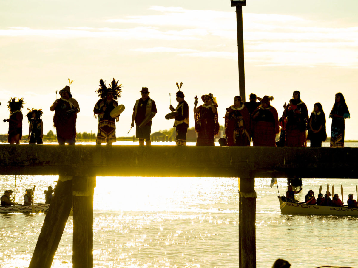 A photo of a Indigenous peoples holding a ceremony as the sun sets on the west coast in 2018.