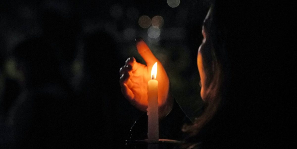 A photo of someone holding a lit candle in the darkness, at a vigil.