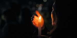 A photo of someone holding a lit candle in the darkness, at a vigil.