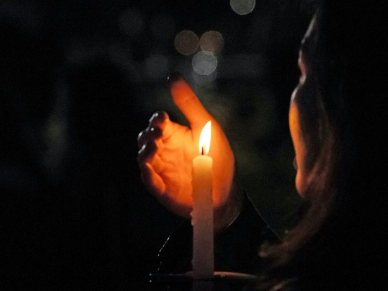 A photo of someone holding a lit candle in the darkness, at a vigil.