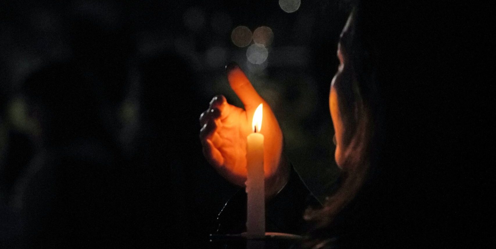 A photo of someone holding a lit candle in the darkness, at a vigil.