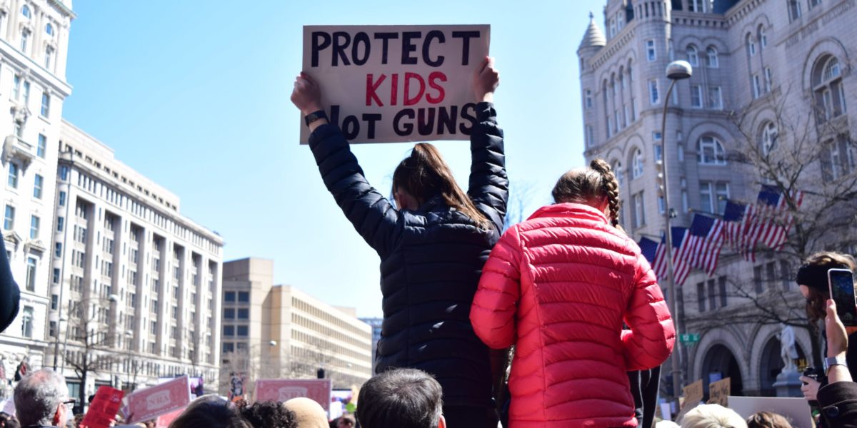 A photo of a person holding up a sign which reads; "Protect kids not guns"