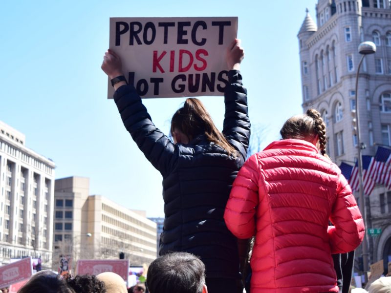 A photo of a person holding up a sign which reads; "Protect kids not guns"