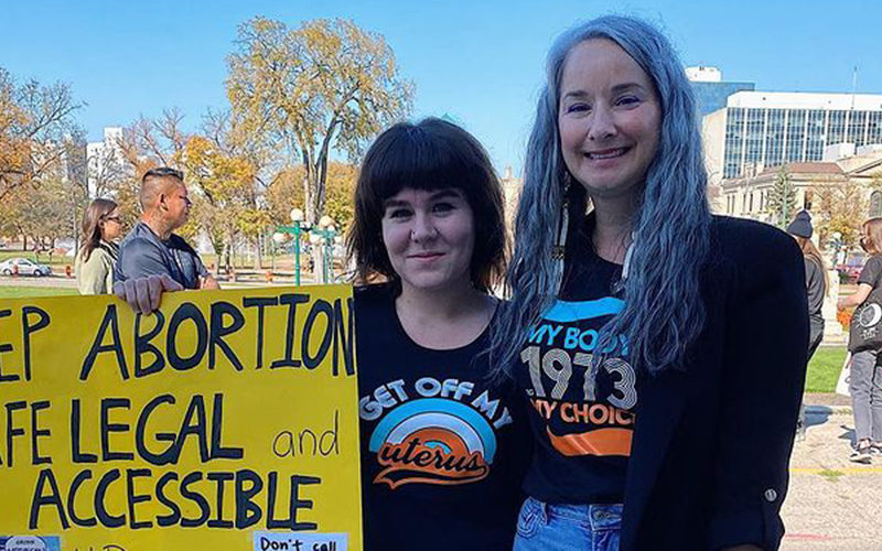 How to lobby politicians. Photo of Paige Mason holding a sign reading Keep abortion safe, legal and accessible with Nahanni Fontaine (NDP MLA for St. Johns Manitoba) at a pro-choice rally outside the Manitoba Legislature in 2021.