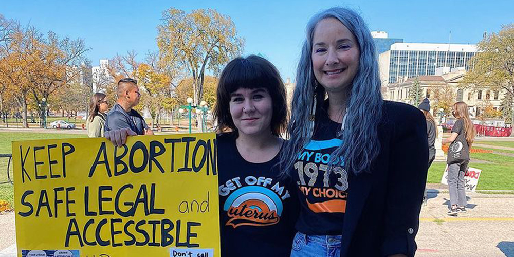 How to lobby politicians. Photo of Paige Mason holding a sign reading Keep abortion safe, legal and accessible with Nahanni Fontaine (NDP MLA for St. Johns Manitoba) at a pro-choice rally outside the Manitoba Legislature in 2021.