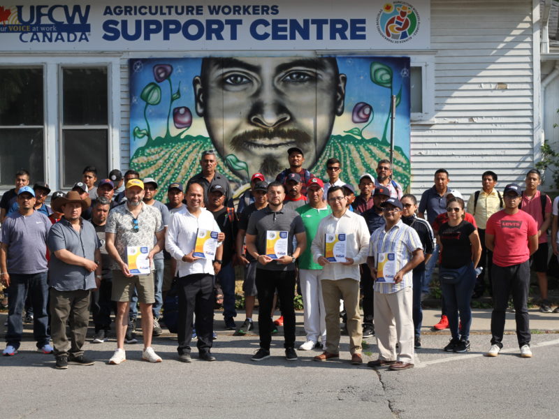 Photo of migrant farm workers standing in front of the Agricultural Workers Support Centre in Lemington, Ontario for the release of the 2022 Migrant Agricultural Workers Report.