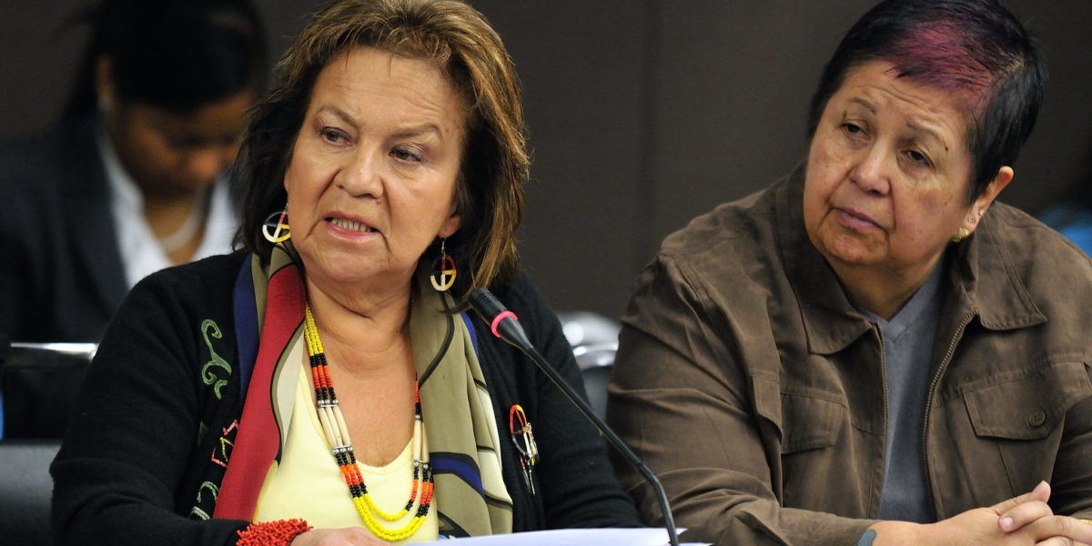 Two seated people at a conference. One is speaking into a microphone.