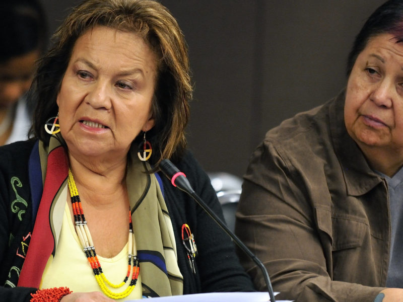 Two seated people at a conference. One is speaking into a microphone.