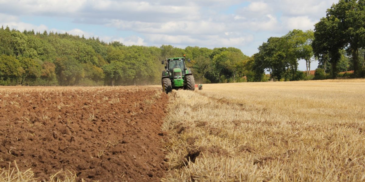 A photo of a farmer working a field in his tractor.