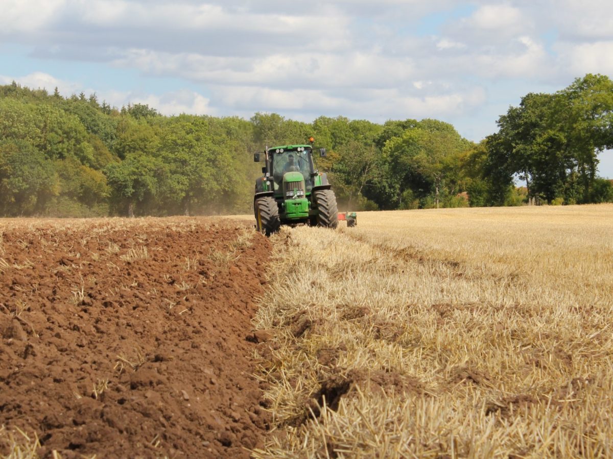 A photo of a farmer working a field in his tractor.