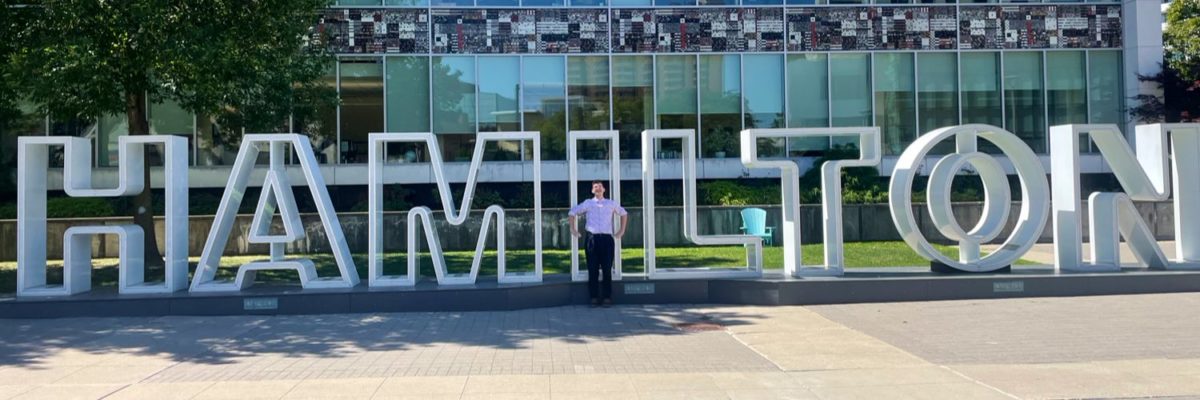 A photo of Alex Wilson in front of the City of Hamilton sign.