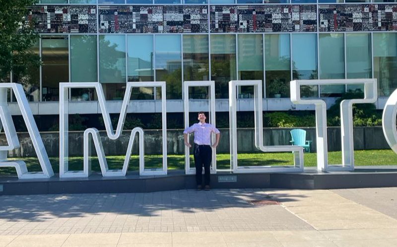 A photo of Alex Wilson in front of the City of Hamilton sign.