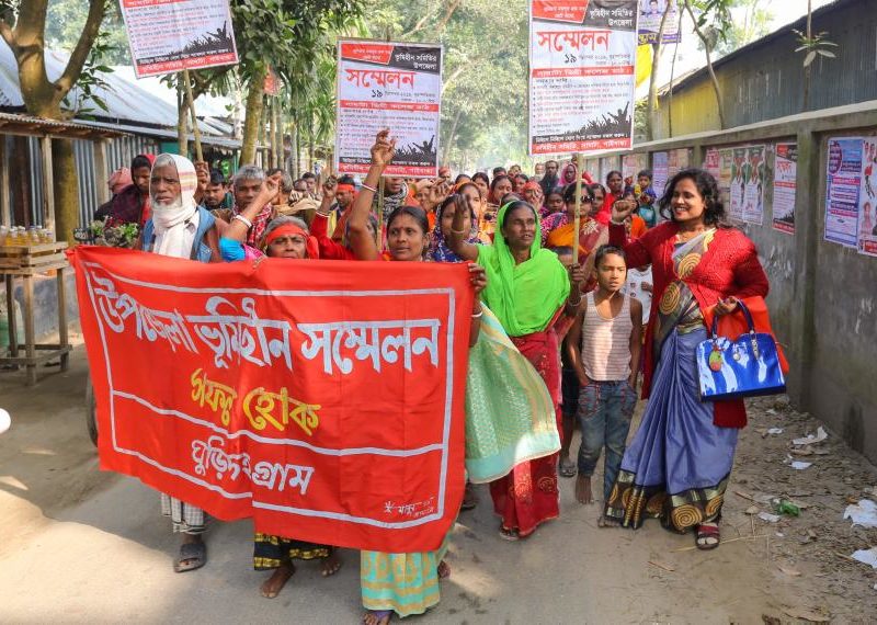 Nijera Kori women protesting in Bangladesh carrying a large red banner in the street.