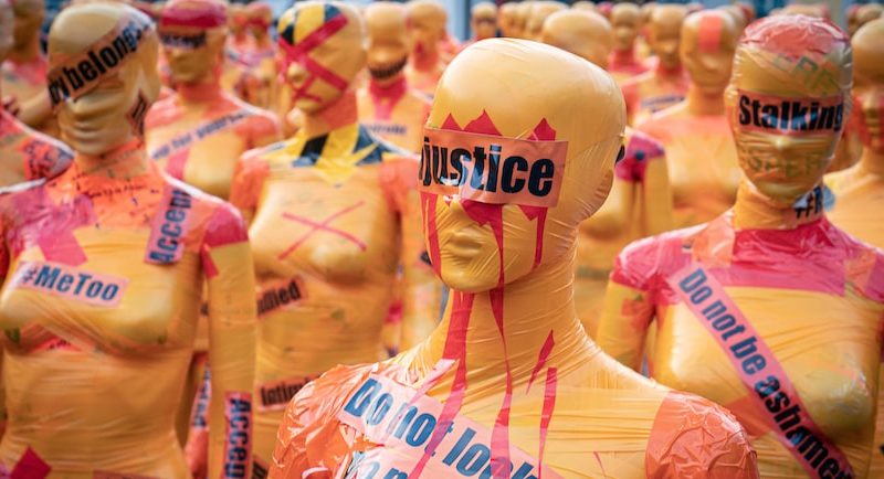 An image of orange mannequins with words on them that say, "Justice," "Do not look away," and "Do not be ashamed"