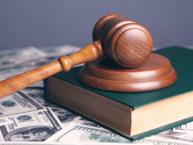 An image of a gavel laying on a book over a pile of money.