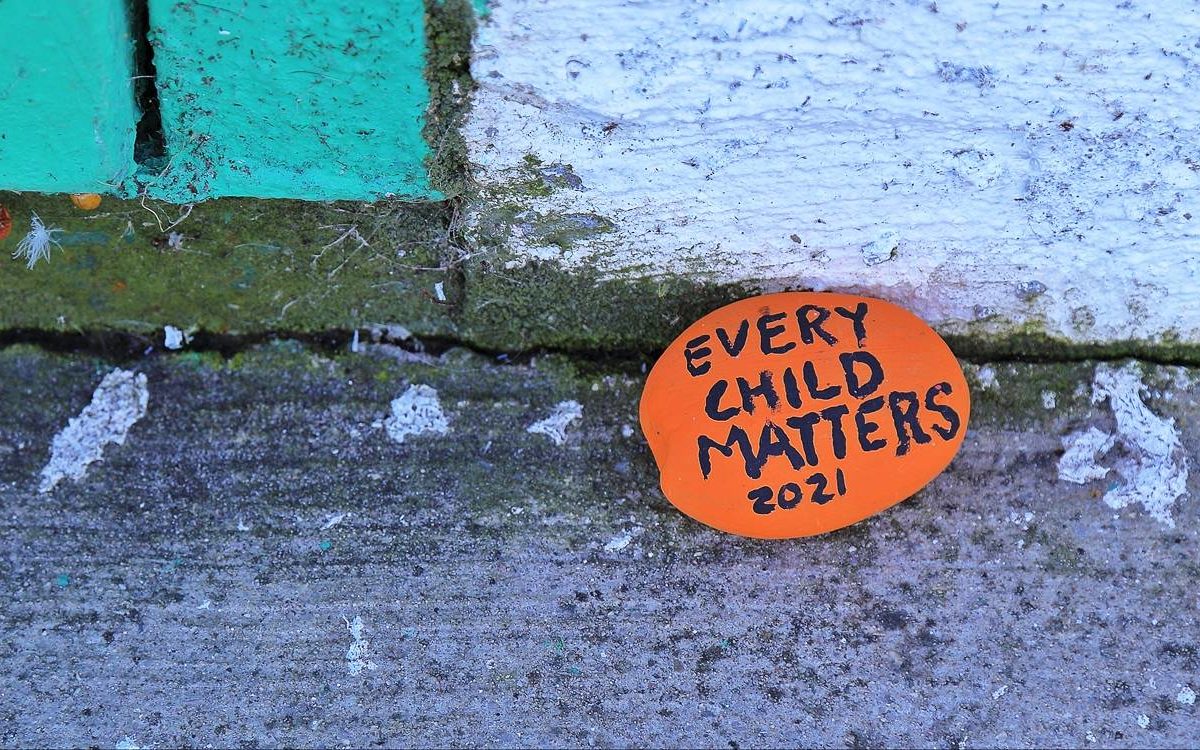 A stone painted in orange with the words Every Child Matters 2021.