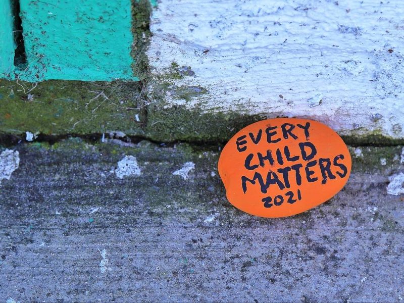 A stone painted in orange with the words Every Child Matters 2021.