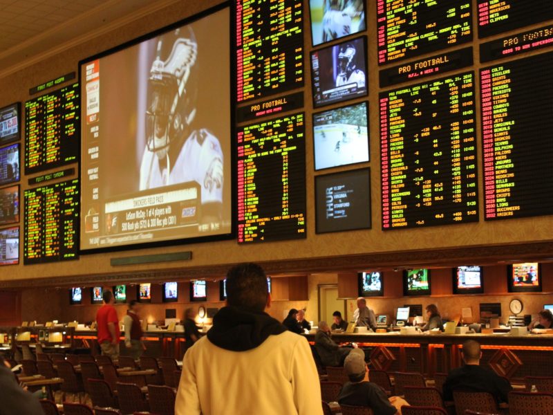 A photo of a person standing in front of an odds board at a race and sports gambling book in Las Vegas.
