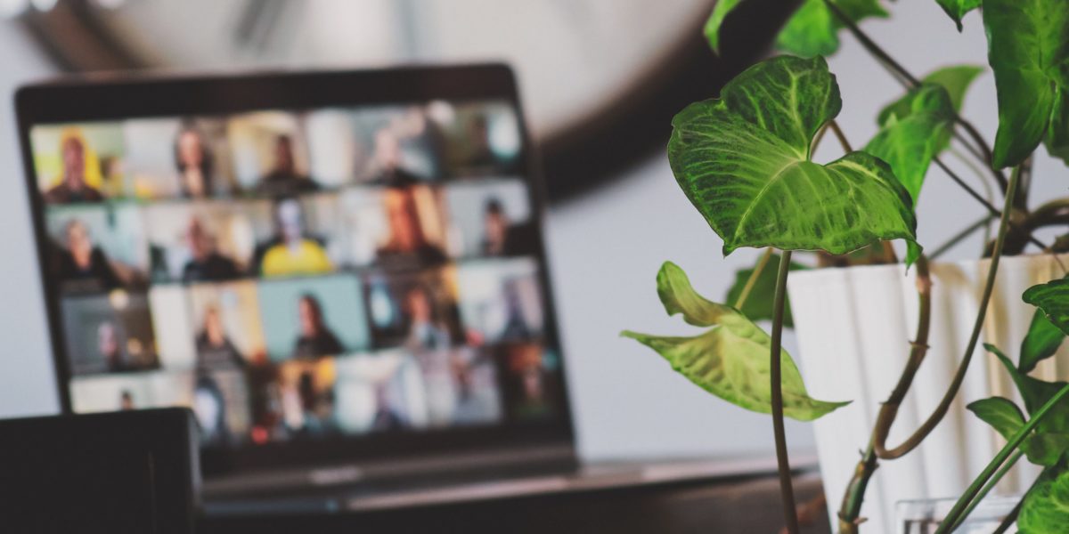 In the background a remote work meeting takes place over a virtual conference call.