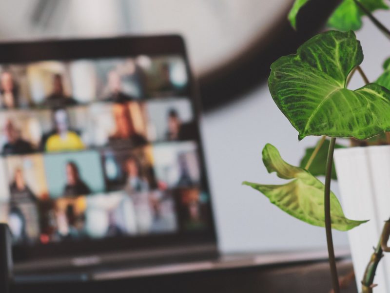 In the background a remote work meeting takes place over a virtual conference call.