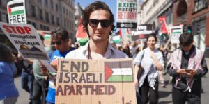 A protester holding a sign calling for the end of the apartheid practices of Israel's government.