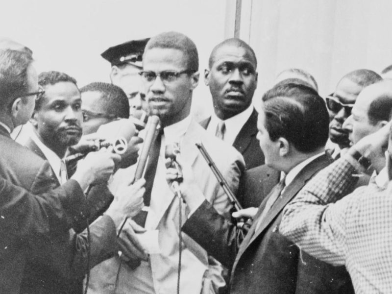 A photo of Malcolm X being interviewed by reporters.