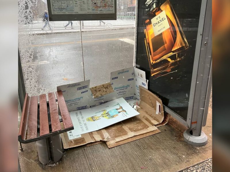 A bed of cardboard boxes inside of a bus shelter.