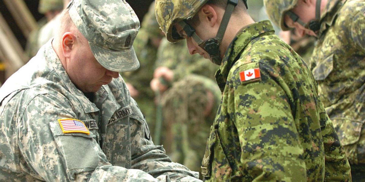 An American soldier training a Canadian soldier.