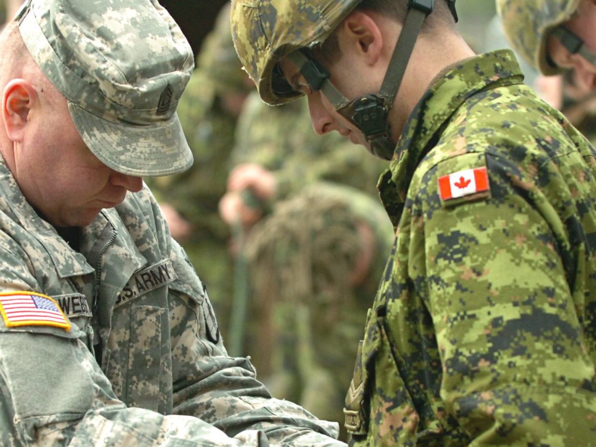 An American soldier training a Canadian soldier.